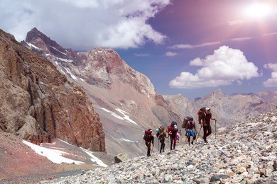 group of mountaineer walking on deserted rocky terrain five members team sport clothing going heavy load backpacks climbing gear up  mountain peaks blue sky majestic summits shining sun background