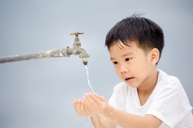 young asian boy use water from old faucet to wash his face and hair on grey cloud on the sky before rain.