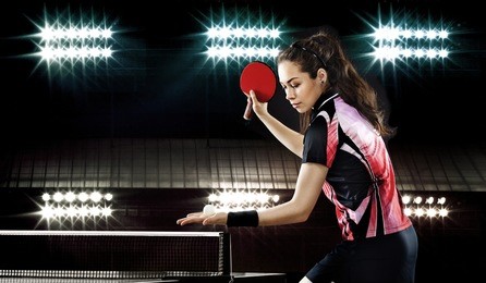 portrait of young woman playing tennis on black background with lights