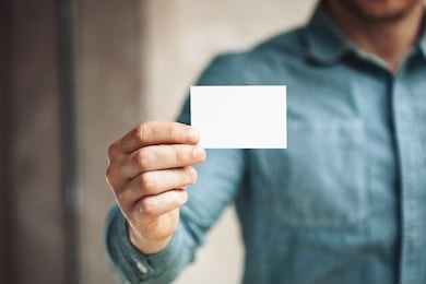 man holding white business card on concrete wall background