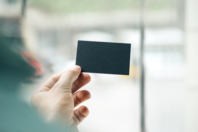 male hand holding black business card on the window background