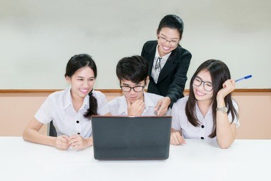asian teacher assisting student using laptop at desk in classroom