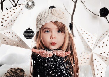 a young child is blowing white snowflakes in a studio background scene with stars and christmas ornaments for a holiday concept.