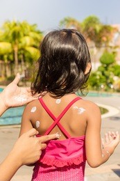 mother hand putting sunscreen lotion on little girl back skin before swimming
