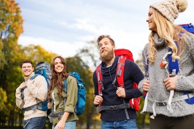 adventure, travel, tourism, hike and people concept - smiling friends walking with backpacks over natural background