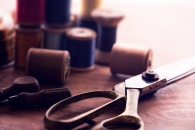old sew thread wooden reels or bobbins on a old grungy work table with scissors. tailor's work table. textile or fine cloth making. shallow depth of field. intentionally shot in nostalgic muted tone.