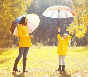 happy family with umbrellas in sunny autumn rainy day, mother and child enjoying rain