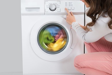 close-up of young woman pressing button of washing machine in kitchen