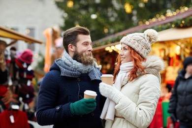 holidays, winter, christmas, hot drinks and people concept - happy couple of tourists in warm clothes drinking coffee from disposable paper cups in old town