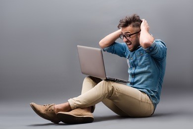 handsome hipster man keeping his head with both hands. obviously, this man made a mistake on his laptop computer.