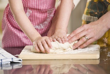 a young child is helping a woman knead some dough to make bread.  horizontally framed shot.