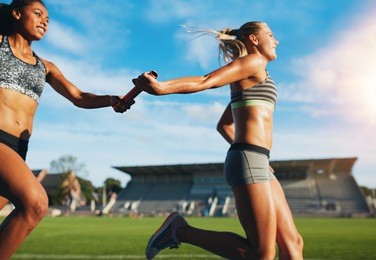 female athletes passing over the baton while running on the track. young women run relay race, track and field event.