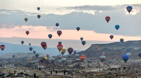 hot air balloons (atmosphere ballons) flying over mountain landscape in the  cappadocia at sunrise, unesco world heritage site since 1985) - turkey
