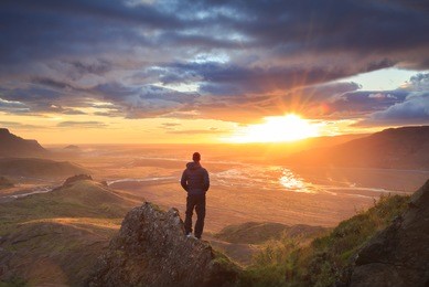 man standing on a ledge of a mountain, enjoying the beautiful sunset over a wide river valley in thorsmork, iceland.
