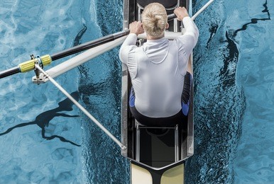 top view of athletic competition rower, who strokes his  paddle through metallic blue water.
