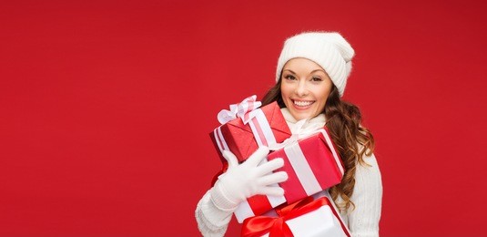 christmas, x-mas, winter, happiness concept - smiling woman in sweater and hat with many gift boxes