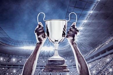 cropped hand of athlete holding trophy against football stadium