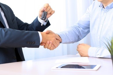 car salesman handing over the keys for a new car to a young businessman . handshake between two business people. focus on a key