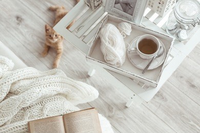 still life details, cup of tea on retro vintage wooden tray on a coffee table in living room, top view point. lazy winter weekend with a book on the sofa.