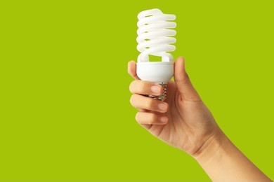 energy saving concept. woman hand holding light bulb on green background.