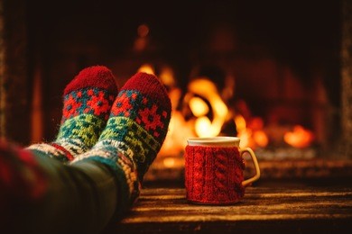 feet in woollen socks by the christmas fireplace. woman relaxes by warm fire with a cup of hot drink and warming up her feet in woollen socks. close up on feet. winter and christmas holidays concept.