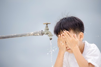 young asian boy use water from old faucet to wash his face and hair on grey cloud on the sky before rain.