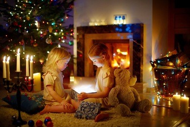 adorable little girls opening a magical christmas gift by a christmas tree in cozy living room in winter