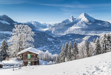 panoramic view of idyllic winter wonderland mountain scenery with traditional mountain chalet in the alps on a sunny day with blue sky