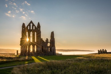 sun star on whitby abbey / the gothic ruins of whitby abbey with the suns rays producing a star.  sea mist held back by the cliffs at sandsend in the background