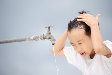 young asian boy use water from old faucet to wash his face and hair on grey cloud on the sky before rain.