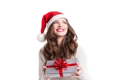 young happy woman in santa hat looking sideways showing christmas present isolated on white background.
