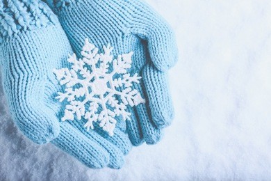 female hands in light teal knitted mittens with sparkling wonderful snowflake on a white snow background. winter and christmas cozy concept.
