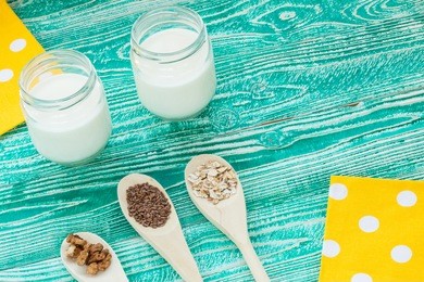 yogurt with wooden spoons with  flax seeds, walnut kernel, cereals, oat-flakes  on yellow napkin at white polka dots on turquoise colored wooden table. top view. copy space, free space for your text.