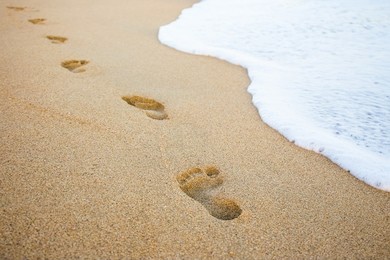 close up of footprints in the sand and sea wave