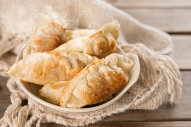 fresh pan fried dumplings on bowl with hot steams. asian dish on rustic vintage wooden background.