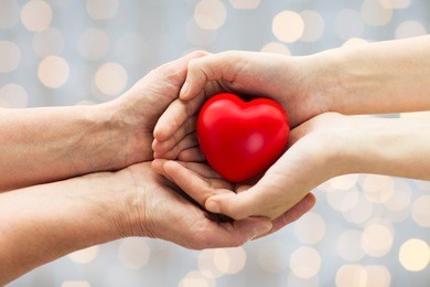 people, age, family, love and health care concept - close up of senior woman and young woman hands holding red heart over lights background