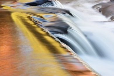 bond falls cascade captured with motion blur and illuminated by reflected color from sunlit autumn foliage and blue sky overhead, michigan's upper peninsula, usa