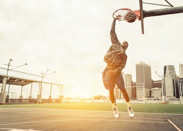 street basketball player performing power slum dunk. manhattan and new york city in the background