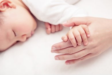 hand of sleeping baby in the hand of mother close-up on the bed, new family and baby protection from mom concept