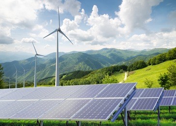 solar panels with wind turbines against mountanis landscape against blue sky with clouds 