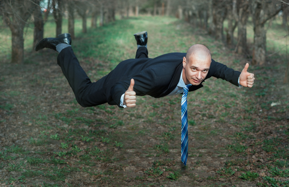 man in a suit flying in the park. his hands showing sign of okay.