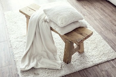 still life details, stack of white cushions and blanket on rustic bench on white carpet