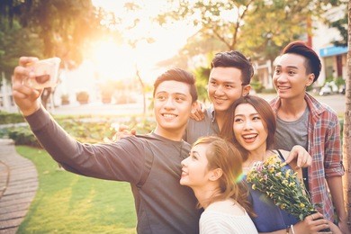 cheerful teenage friends taking selfie against sunset