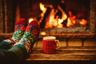 feet in woollen socks by the christmas fireplace. woman relaxes by warm fire with a cup of hot drink and warming up her feet in woollen socks. close up on feet. winter and christmas holidays concept.