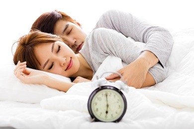 young  couple sleeping in bed next to an alarm clock