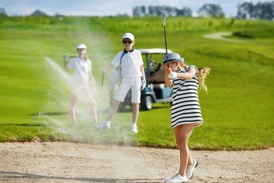 girl playing golf and  hitting from bunker 