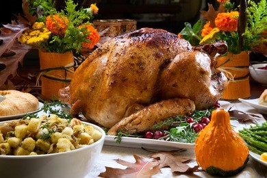 roasted turkey garnished with cranberries on a rustic style table decoraded with pumpkins, gourds, asparagus, brussel sprouts, baked vegetables, pie, flowers, and candles.
