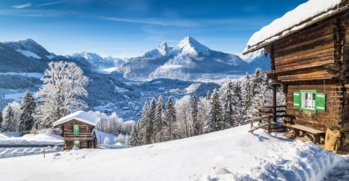 panoramic view of beautiful white winter wonderland mountain scenery in the alps with traditional mountain chalets on a cold sunny day with blue sky and clouds 
