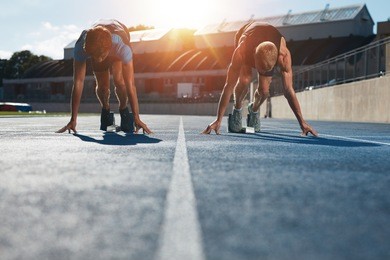 sprinters at starting blocks ready for race . athletes at starting position on athletics stadium race track with sun flare.