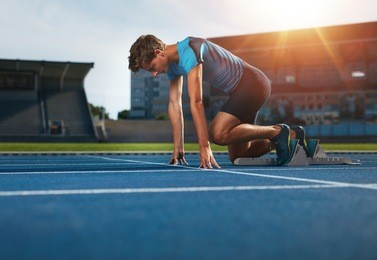 young athlete at starting position ready to start a race. male runner ready for sports exercise on racetrack with sun flare.